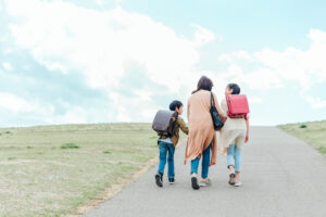 お母さんと二人の小学生が一緒に歩いている後ろ姿の写真